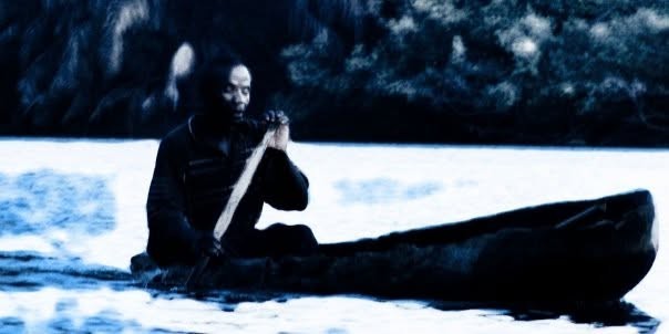 We're all in the same boat: a man paddling a dugout canoe on a river, in cold blue light